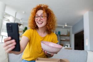 jong tevreden gelukkig vrouw shopaholic klant zitten Aan sofa uitpakken pakket levering doos, online boodschappen doen Verzending concept. nemen foto's van Product naar post Aan sociaal media foto