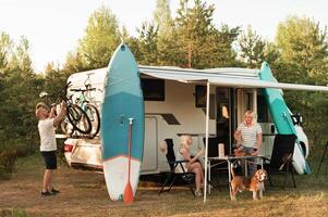 een gelukkig familie is resting dichtbij in de buurt hun camper in de Woud foto