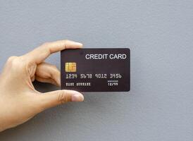 vrouw hand- Holding een zwart credit kaart mockup met veiligheid spaander ingebed Aan een grijs achtergrond foto