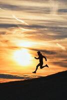 sportief Mens loopt naar beneden heuvel in silhouet foto