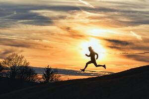 sportief Mens loopt naar beneden heuvel in silhouet foto