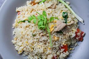 gebakken rijst- met varkensvlees en groenten in een bord Aan de tafel foto