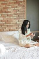 jong mooi en gelukkig Aziatisch Chinese vrouw in slaapkamer en bril gebruik makend van mobiel telefoon in bed Bij huis slaapkamer in internet verslaving en sociaal media verslaving concept foto