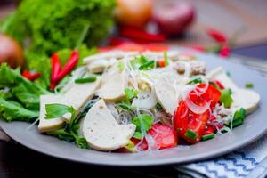 pittig glas noodle salade met Vietnamees worst geserveerd in een grijs bord zetten Aan een houten tafel en divers groenten. foto