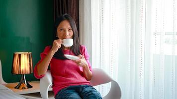 portret van mooi jong Aziatisch vrouw Holding kop van ochtend- koffie in wit slaapkamer, Vrolijk, vrolijk, ontspannende in zomer. Thais Aziatisch bedenken ideeën, wit slaapkamer foto