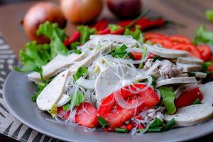 pittig glas noodle salade met Vietnamees worst geserveerd in een grijs bord zetten Aan een houten tafel en divers groenten. foto