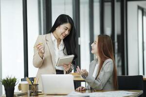 twee bedrijf Dames zijn bespreken de werk ze hebben gedaan samen en uitwisselen ideeën. naar werk naar ontwikkelen de bedrijf beter. foto