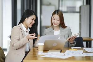 twee bedrijf Dames zijn bespreken de werk ze hebben gedaan samen en uitwisselen ideeën. naar werk naar ontwikkelen de bedrijf beter. foto