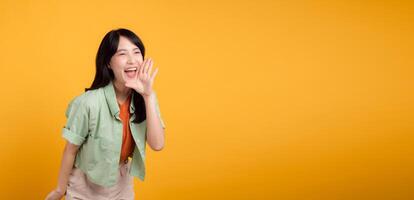 levendig jong Aziatisch vrouw in haar Jaren 30 vervelend een groen en oranje shirt, energiek geschreeuw met haar mond geïsoleerd Aan een geel achtergrond. onderzoeken de korting boodschappen doen Promotie concept. foto