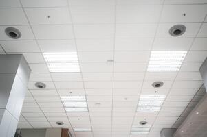 plafond gemonteerd cassette type lucht conditioner en modern lamp licht Aan wit plafond. kanaal lucht conditioner voor huis, hal of kantoor. foto