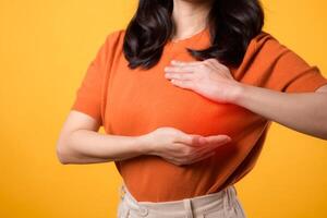 vrouw handen controle knobbeltjes Aan haar borst voor tekens van borst kanker Aan geel achtergrond. gezondheidszorg wereld Gezondheid dag concept. foto