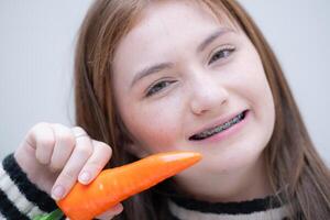 portret van tiener- meisje aan het eten wortel in haar tanden. foto