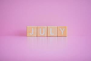 houten blokken het formulier de tekst juli tegen een roze achtergrond. foto