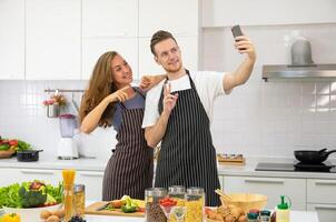 jong paar minnaar Koken samen in de keuken Bij huis. gelukkig paar nemen selfie met smartphone. foto