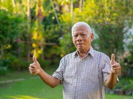 vrolijk senior Mens tonen duim omhoog gebaar door twee handen over- in zijn tuin foto