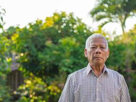 portret van een senior Mens op zoek Bij de camera terwijl staand in een tuin foto