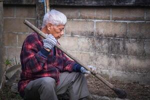 een senior Mens gebruik een schoffel naar Schep de bodem terwijl zittend in de tuin foto