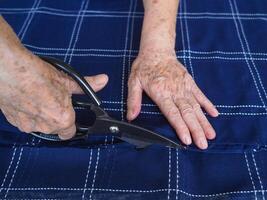 detailopname gedeeltelijk visie van oud vrouw handen snijdend kleding stof met schaar. foto