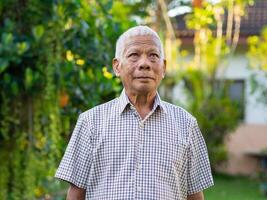 portret van een senior Mens glimlachen en op zoek omhoog terwijl staand in een tuin foto