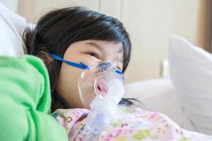 ziek weinig Aziatisch meisje inademing met vernevelaar voor ademhalings behandeling foto