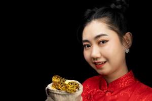 portret Aziatische jonge, vrouw rode jurk traditionele cheongsam met een gouden munt in een zak op de zwarte achtergrond foto