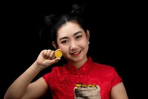 portret Aziatische jonge, vrouw rode jurk traditionele cheongsam met een gouden munt in een zak op de zwarte achtergrond foto