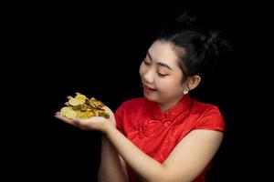portret Aziatische jonge vrouw rode jurk traditionele cheongsam met een gouden munt op zwarte achtergrond