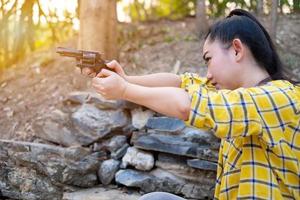 portret de boer asea vrouw draagt een shirt bij de schietpartij schot van een oud revolvergeweer in de boerderij, jong meisje zittend in de houding van richten en kijkend door het zichtpistool foto