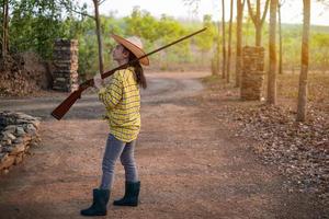 portret de boer asea vrouw draagt een hoed hand met snuit-ladend vintage pistool in de boerderij, jong meisje met luchtgeweer een tuin foto