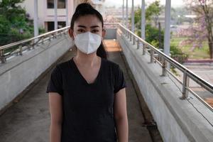 close-up van een vrouw die een gasmasker opzet n95-masker ter bescherming tegen luchtwegaandoeningen als griep covid-19 coronavirus ebola pm2.5 stof en smog op de weg braamachtergrond foto