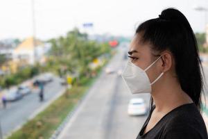 close-up van een vrouw die een gasmasker opzet n95-masker ter bescherming tegen luchtwegaandoeningen als griep covid-19 coronavirus ebola pm2.5 stof en smog op de weg braamachtergrond foto