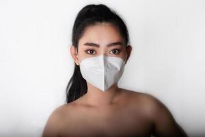 close-up van jonge aziatische vrouw die een medisch masker n95 opzet om te beschermen tegen luchtwegaandoeningen als griep covid-19 pm2.5 stof en smog op grijze achtergrond, veiligheidsvirusinfectieconcept foto