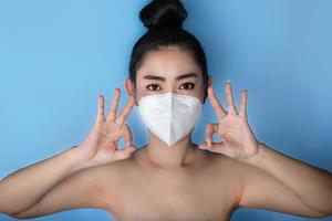 close-up van een vrouw die een respirator n95-masker opzet ter bescherming tegen luchtwegaandoeningen als griep covid-19 corona pm2.5 stof en smog, vrouwelijk duim omhoog gebaar met hand die ok teken toont