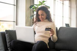 Latijnse vrouw die laptop en hand met creditcard gebruikt om op de bank te winkelen foto