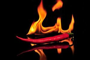 rood pepers brandend in vlammen Aan een zwart glas tafel foto