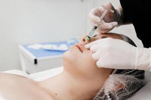 chirurg, in medisch handschoenen, voorzichtig en langzaam injecteert hyaluronzuur zuur in vrouw lippen met een spuit. lip vergroting procedure. schoonheid injecties. plastic chirurgie. foto