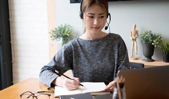 close-up hand van aziatische vrouw die online vanuit huis studeert en aantekeningen maakt voor afstandsonderwijs voor studenten op laptop huiswerk maken, luisteren naar videolessen. onderwijsconcept op afstand. foto