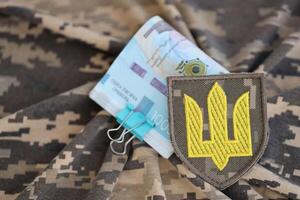 oekraïens leger symbool en bundel van hryvnia rekeningen Aan leger uniform. betalingen naar soldaten van de oekraïens leger, salarissen naar de leger foto