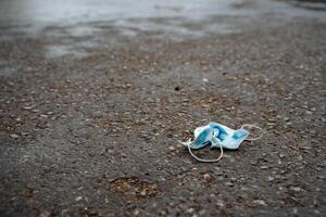 beschermend medisch masker is aan het liegen Leuk vinden vuilnis Aan de asfalt, de gebruikt masker was verpletterd en gegooid weg, medisch afval, foto's Aan de onderwerp van ecologie foto