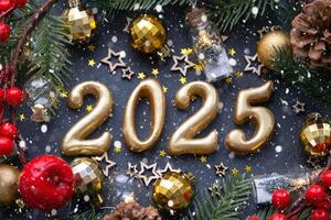 de gouden figuren 2025 gemaakt van kaarsen Aan een zwart steen leisteen achtergrond zijn versierd met een feestelijk decor van sterren, pailletten, Spar takken, ballen en slingers. groet kaart, gelukkig nieuw jaar. foto