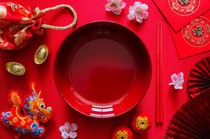 rood bord met eetstokje Aan rood kleding achtergrond met blokken woord gemeen rijkdom, rood tas, draak hanger en rood envelop pakket of ang bao woord gemeen zegen voor Chinese nieuw jaar avondeten concept. foto