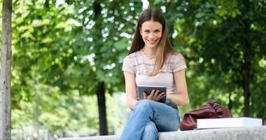 meisje met tablet zittend Aan een park bank foto