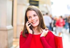 jong vrouw boodschappen doen met een Kerstmis kleding terwijl wandelen en sprekend Aan de telefoon foto