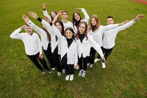 een groep van veel gelukkig tieners gekleed in de dezelfde kleding hebben pret en poseren in een stadion in de buurt een middelbare school. concept van vriendschap, momenten van geluk. school- vriendschap foto