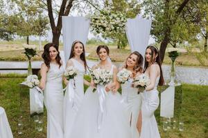 groep portret van de bruid en bruidsmeisjes. bruid in een bruiloft jurk en bruidsmeisjes in wit jurken en Holding elegant boeketten Aan de bruiloft dag tegen de achtergrond van de meer. foto