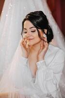 een mooi brunette bruid met een tiara in haar haar- is krijgen klaar voor de bruiloft in een mooi gewaad in boudoir stijl. detailopname bruiloft portret, foto. foto