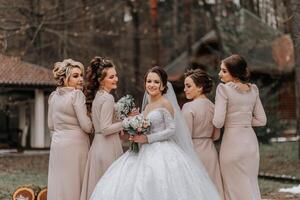 een brunette bruid in een wit elegant jurk en haar vrienden in grijs jurken houding met boeketten. bruiloft portret in natuur, bruiloft foto in licht kleuren.