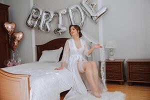 ballonnen bruid en een mooi bruid zittend Aan een bed in een luxueus boudoir jurk voorbereidingen treffen voor de bruiloft ceremonie. foto