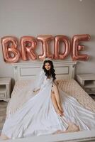 ballonnen bruid en een mooi bruid zittend Aan een bed in een luxueus boudoir jurk voorbereidingen treffen voor de bruiloft ceremonie. foto