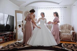 vrienden verheugen met de bruid in de ochtend. ze nemen afbeeldingen, glimlach, helpen de bruid vastmaken haar jurk. foto